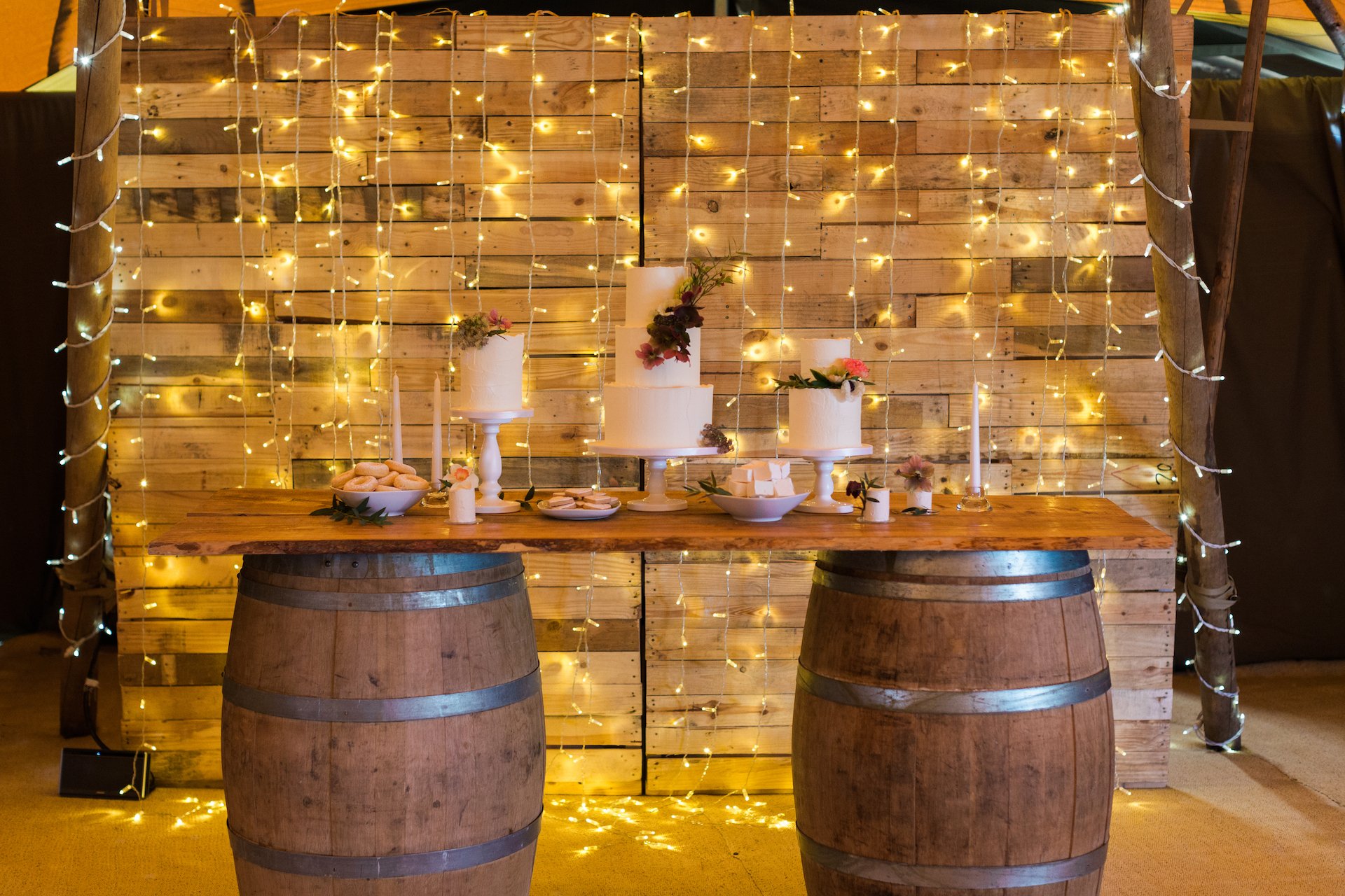 PapaKåta Spring Open Weekend Teepee captured by Lucy Davenport Photography: Wine Barrel Bar with Cake Display by Cherry Blossom Cakes, Fairy Light Baffle Backdrop